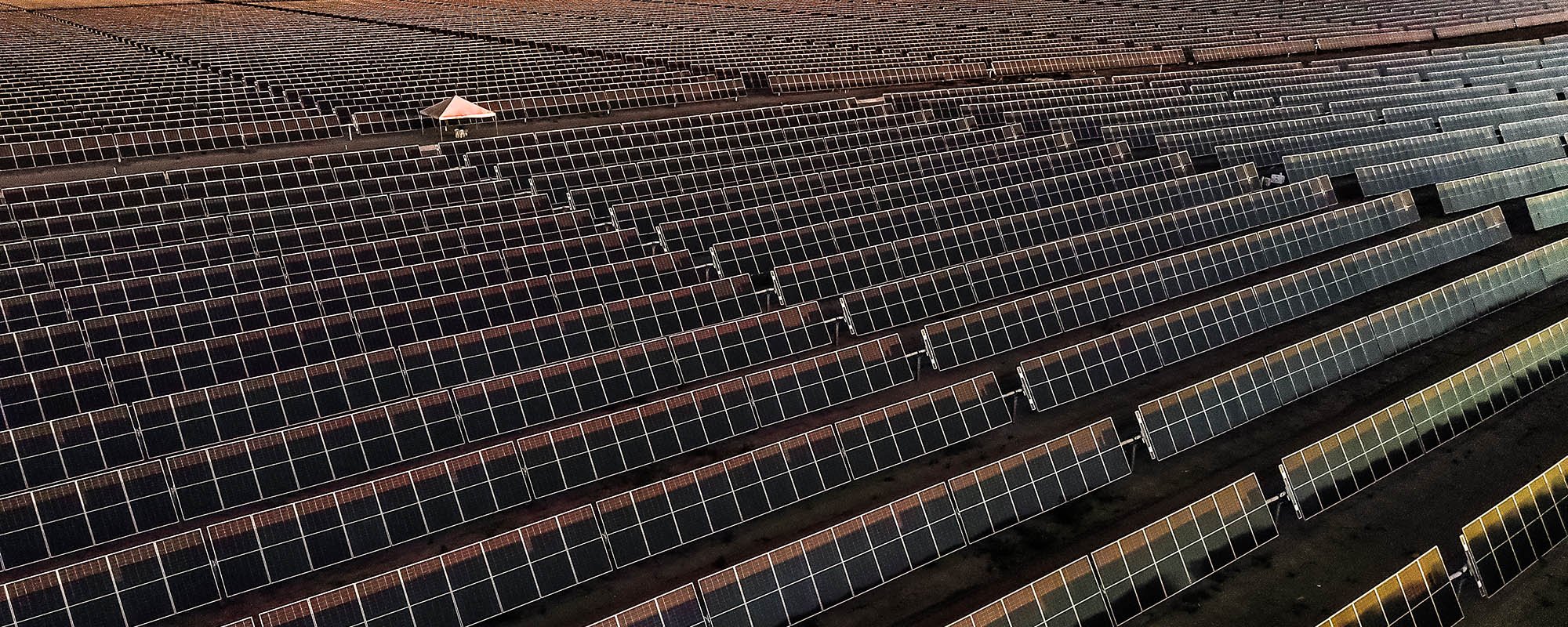 Massive field of dark solar panels extending to the horizon in a desert or arid region.