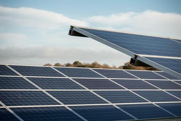 Close-up of solar panels at the Lightsource bp lbstock solar project in the UK, part of their UK Projects portfolio, set against a partly cloudy sky with trees on the horizon.