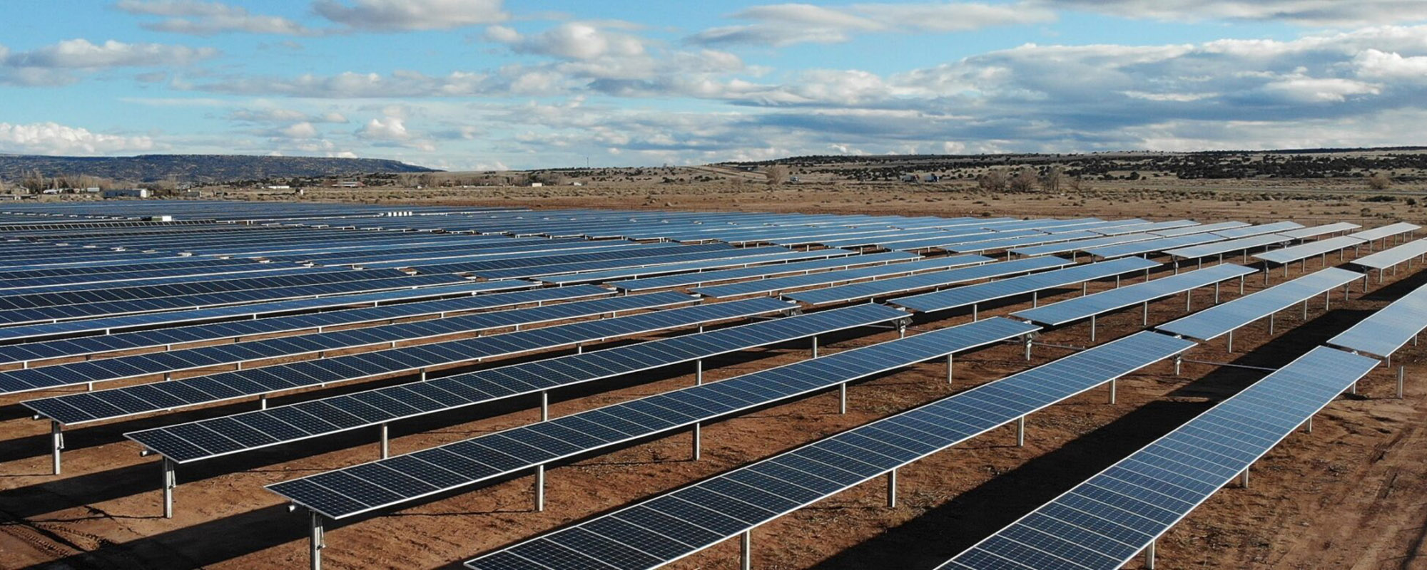 Wide-angle view of the Lightsource bp Grants & Bluewater Solar Farms in New Mexico, part of their US Projects portfolio, rows of solar panels stretch across arid land under a vast blue sky with scattered clouds.
