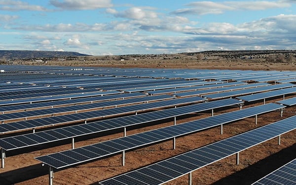 Rows of solar panels at the Lightsource bp Grants & Bluewater Solar Farms in New Mexico, part of their US Projects portfolio, stretching across arid land under a partly cloudy sky.
