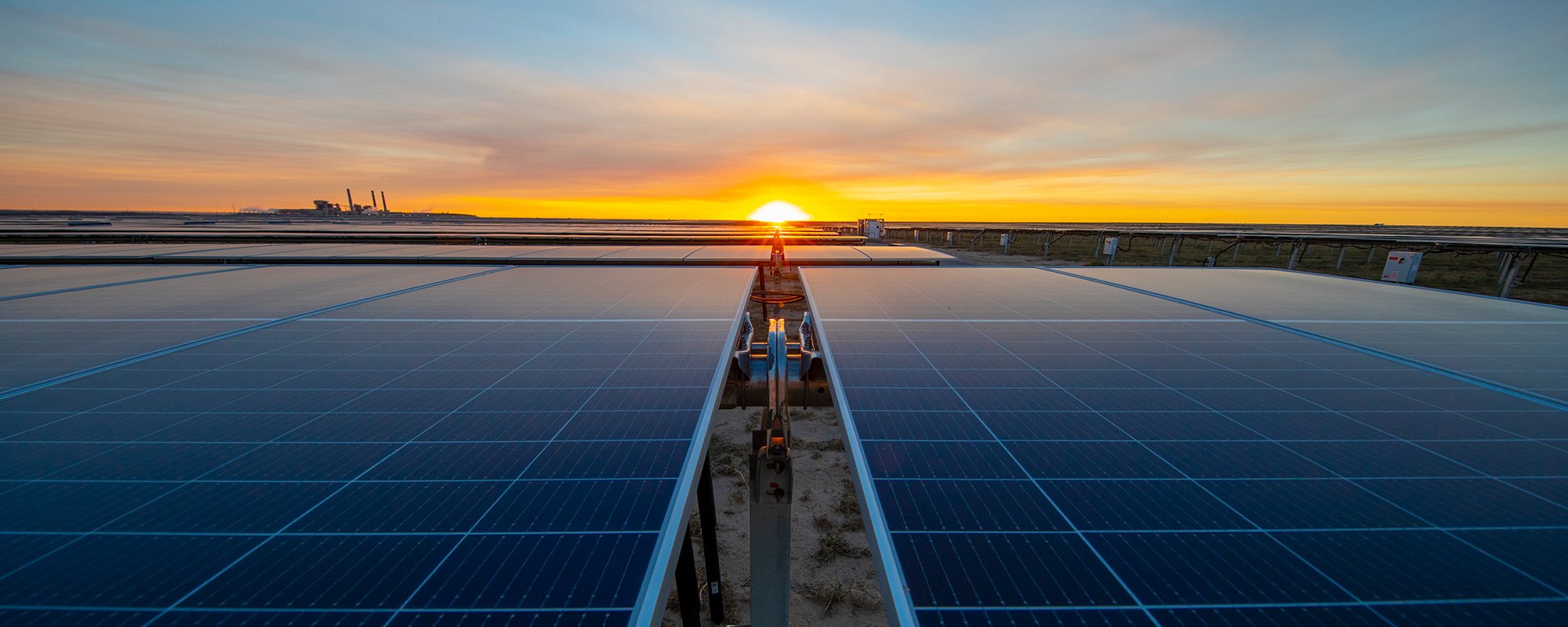 A striking sunset bathes the Lightsource bp Bighorn solar project in warm light, with long rows of panels stretching into the horizon. This US Projects site exemplifies large-scale renewable energy development in America, captured from a ground-level perspective between arrays.