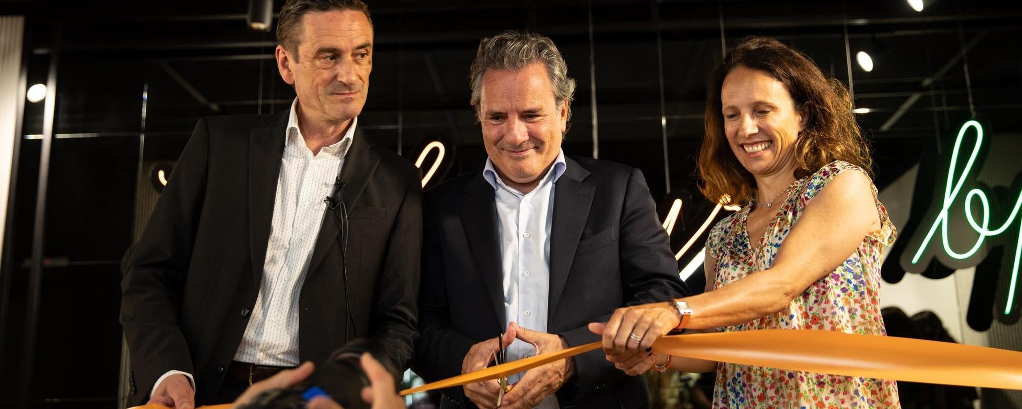 Three people cutting an orange ribbon