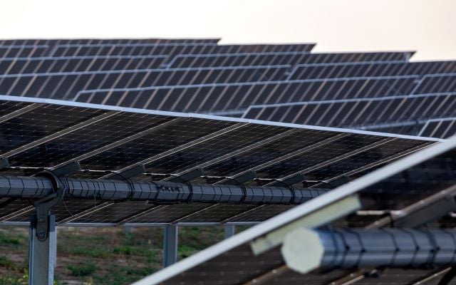Ground-mounted solar panels with tracking technology, focusing on the dark solar cells and the horizontal central torque tube.