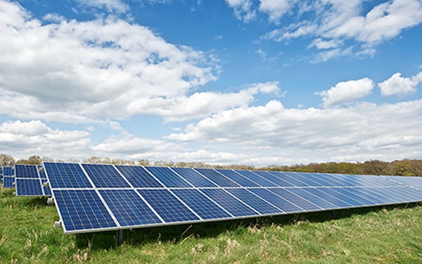 Rows of solar panels at a Lightsource bp solar project, installed across green grass under a bright blue sky with fluffy white clouds.