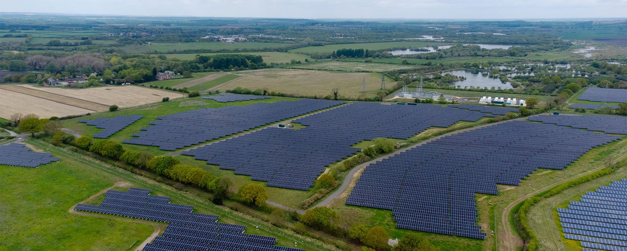 Aerial view of a Lightsource bp solar project in the UK, part of their UK Projects portfolio — vast arrays of panels installed across green fields with water bodies and farmland visible in the distance.