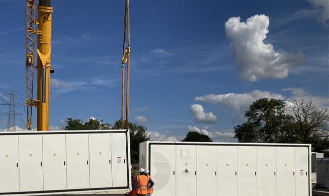 A crane manoeuvring battery storage, a workman in orange PPE