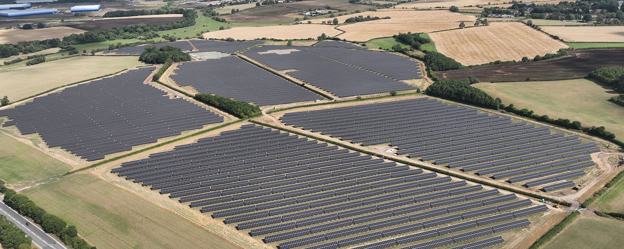Aerial view of the Lightsource bp Streetfields and Northfield House solar project in the UK, part of their UK Projects portfolio, vast arrays of panels installed across green and harvested fields under a clear sky.