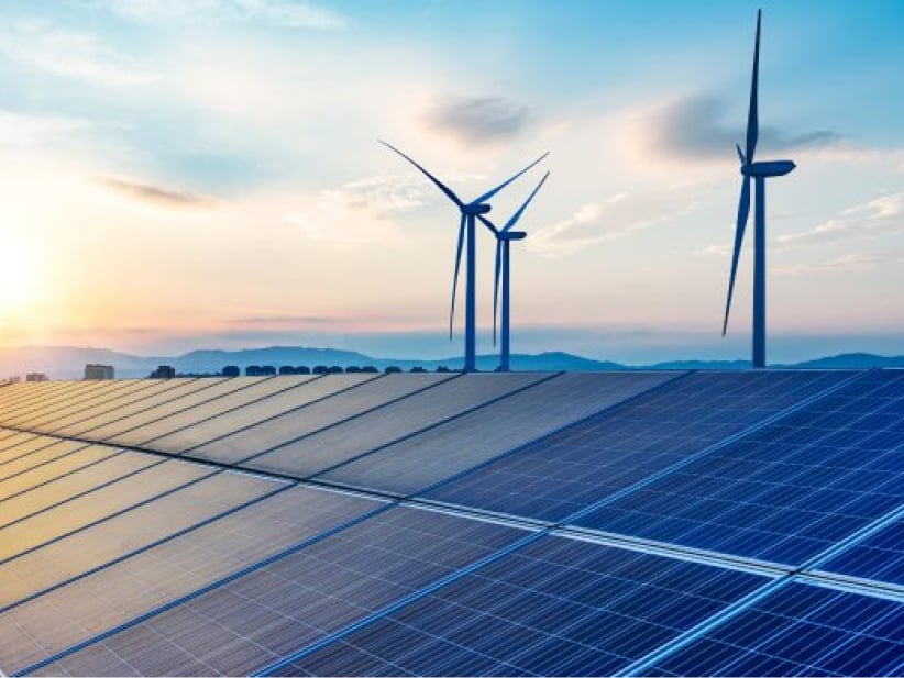 Solar panels in the foreground with wind turbines in the background at sunset