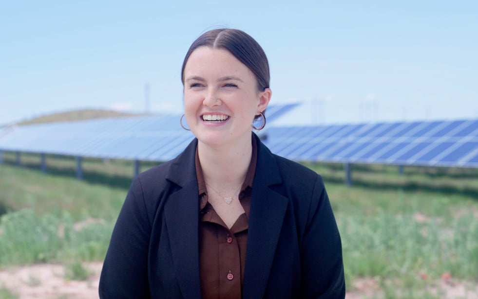 Woman in a suit smiling in a solar farm with solar panels in the background