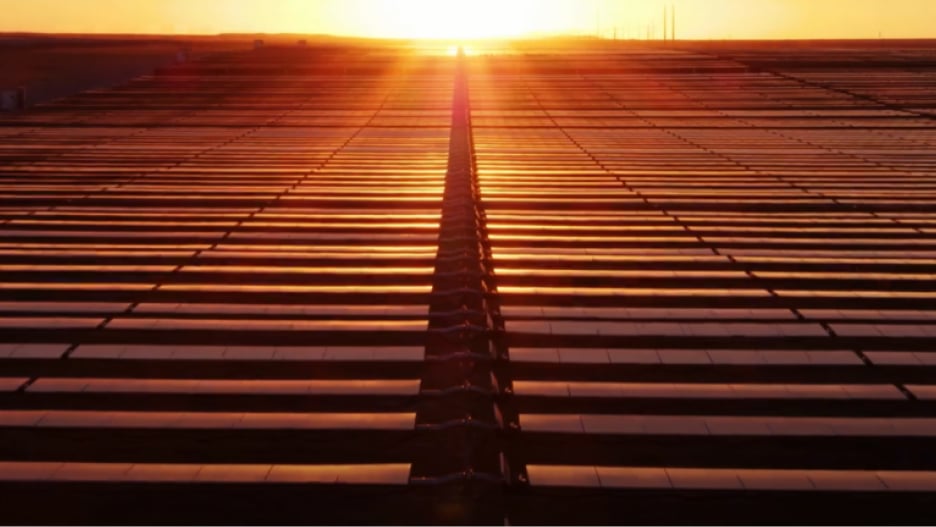 Solar panels reflecting the sunset, with the sun setting directly behind the panels