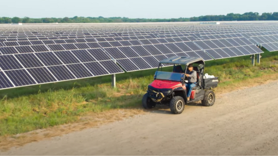 A person driving a utility vehicle on a dirt road next to a large solar farm