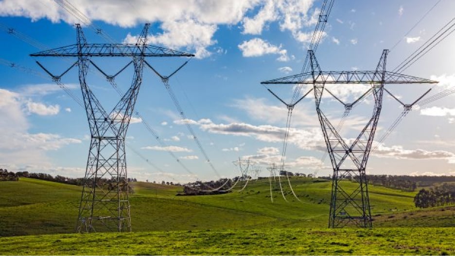 A landscape photo showing a series of power transmission towers and power lines stretching across a rural area.