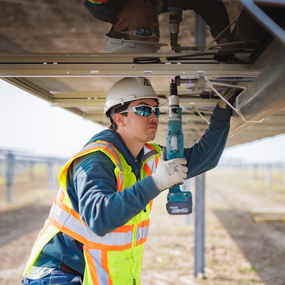 Person in PPE and wearing protective head gear working on solar panels