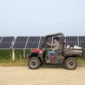 A person driving a utility vehicle through a solar farm, likely for maintenance or inspection purposes.