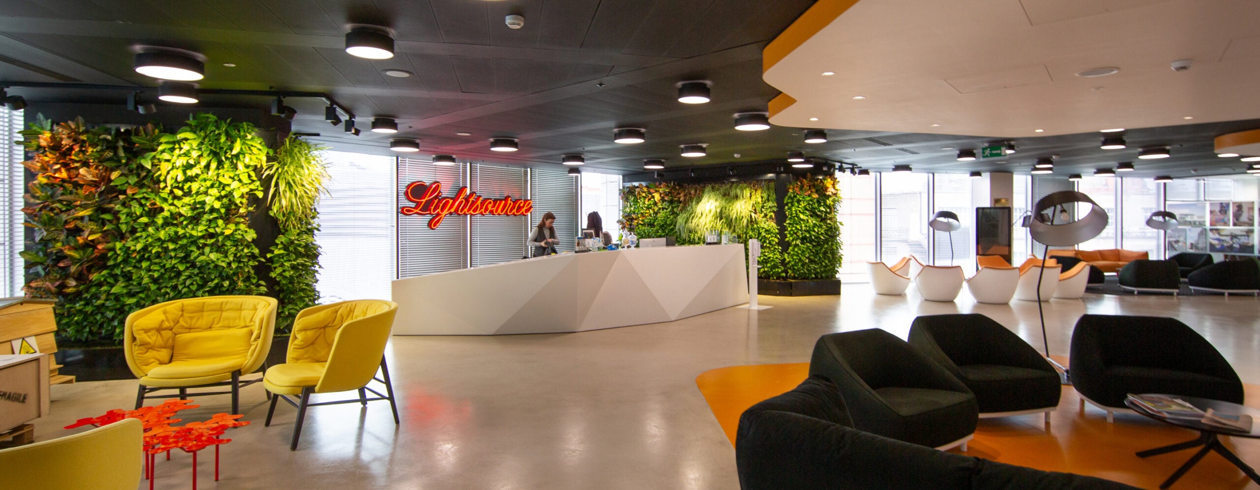Bright and modern office reception area with a white reception desk, comfortable seating, and prominent green walls.