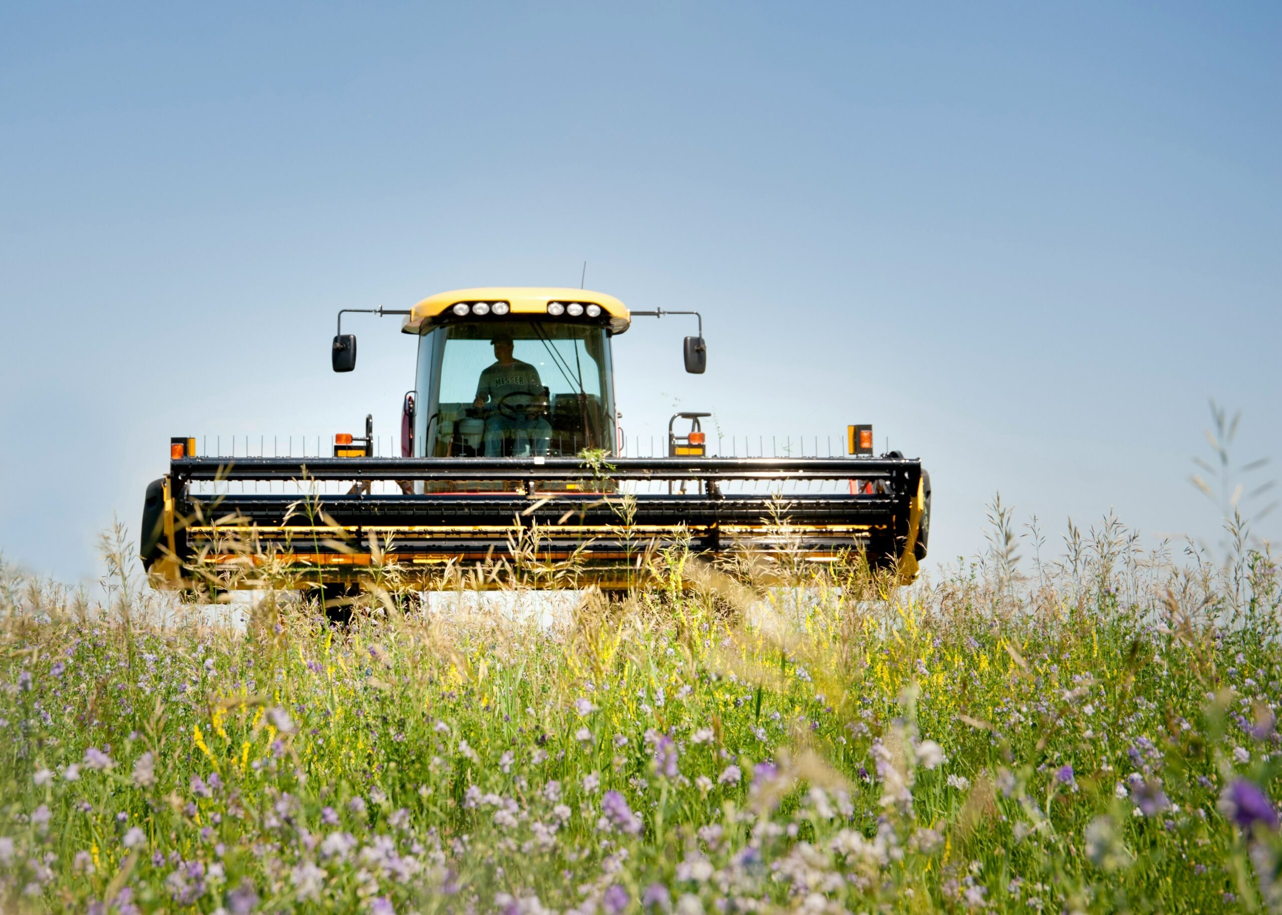 Farm machinery used for harvesting or mowing tall vegetation under a bright blue sky.