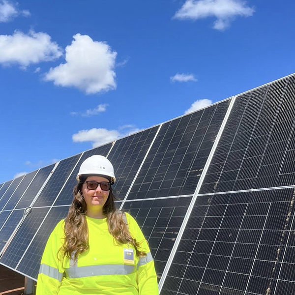 Patricia Batista wearing high vis and hard hat PPE in front of a solar panel