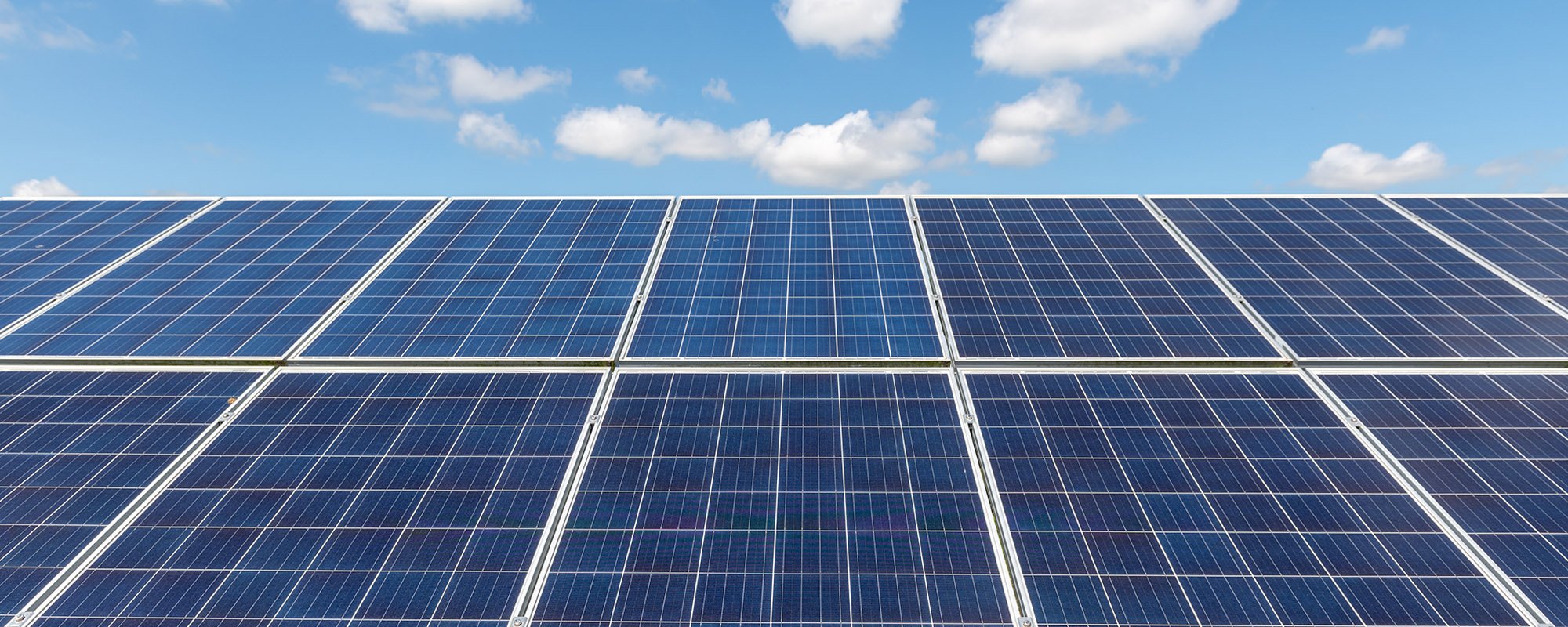 Rows of solar panels at a Lightsource bp solar project, installed under a bright blue sky with fluffy white clouds.