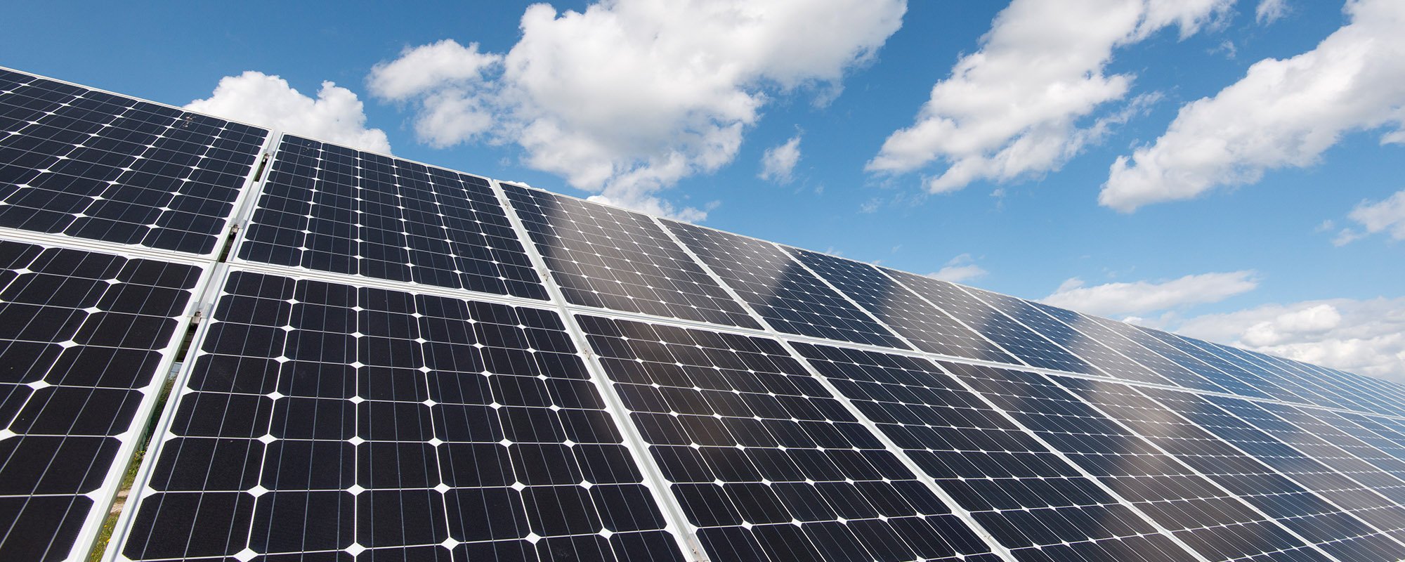 Rows of solar panels at a Lightsource bp solar project, installed under a bright blue sky with fluffy white clouds.