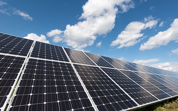 Rows of solar panels at a Lightsource bp solar project, installed under a bright blue sky with fluffy white clouds.
