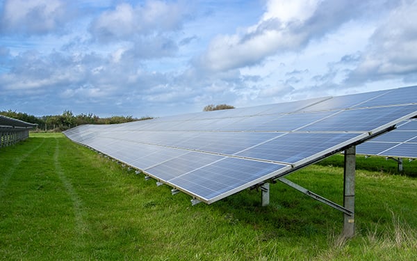 Rows of solar panels at a Lightsource bp solar project, installed across green grass under a partly cloudy blue sky.