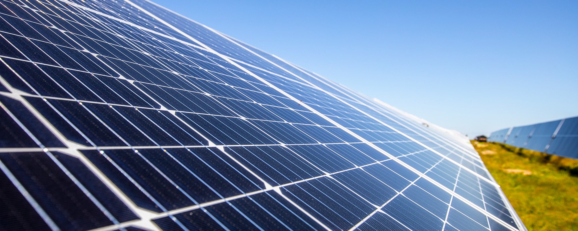 Close-up of a solar panel at a Lightsource bp solar project, angled toward a clear blue sky with green grass visible in the distance.