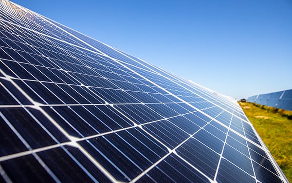 Close-up of a solar panel at a Lightsource bp solar project, angled toward a clear blue sky with green grass visible in the distance.