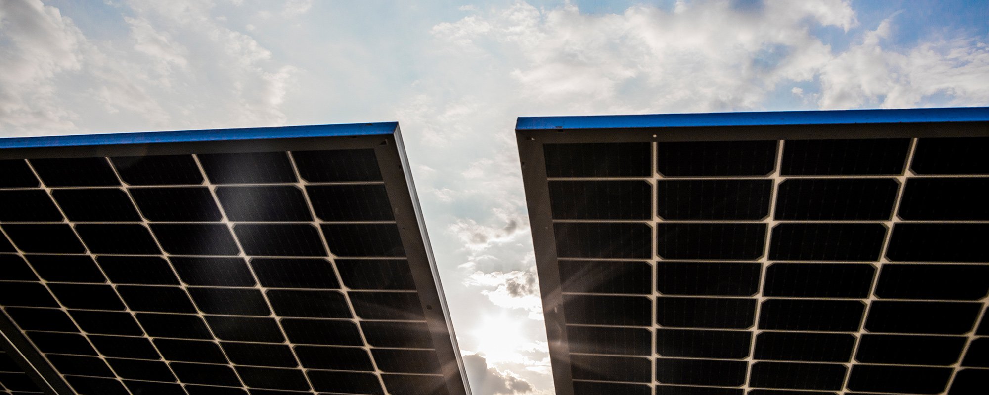 Solar panels at a Lightsource bp solar project, angled toward a bright sky with clouds and sun glare.