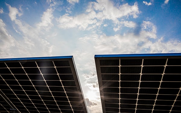 Solar panels at a Lightsource bp solar project, angled toward a bright blue sky with fluffy white clouds and sun glare.