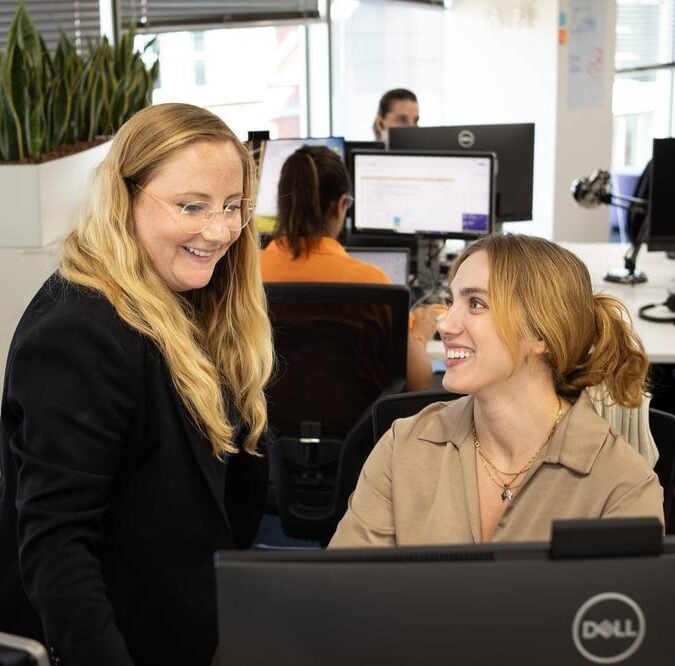 Two women in an office setting, smiling and looking at a computer monitor
