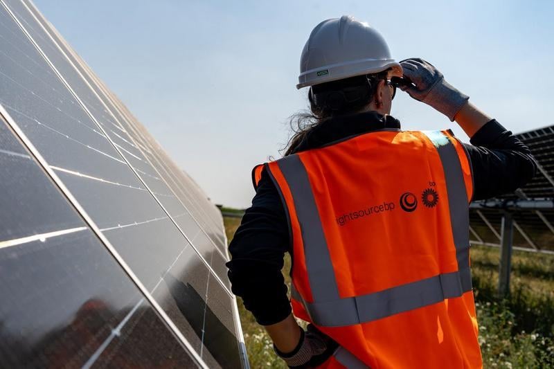 A woman in branded Lightsource bp PPE stood next to solar panels, looking out across the solar farm